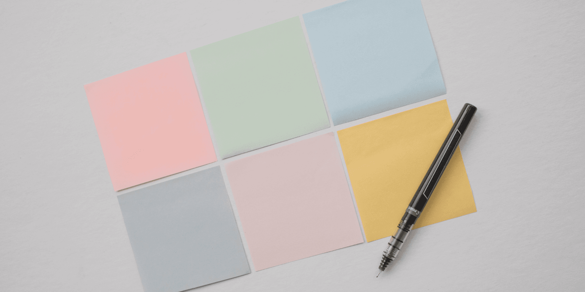 Six pastel sticky notes laid out in a grid on a desk, a pencil resting on them, ready to start a Year in Pixels by hand